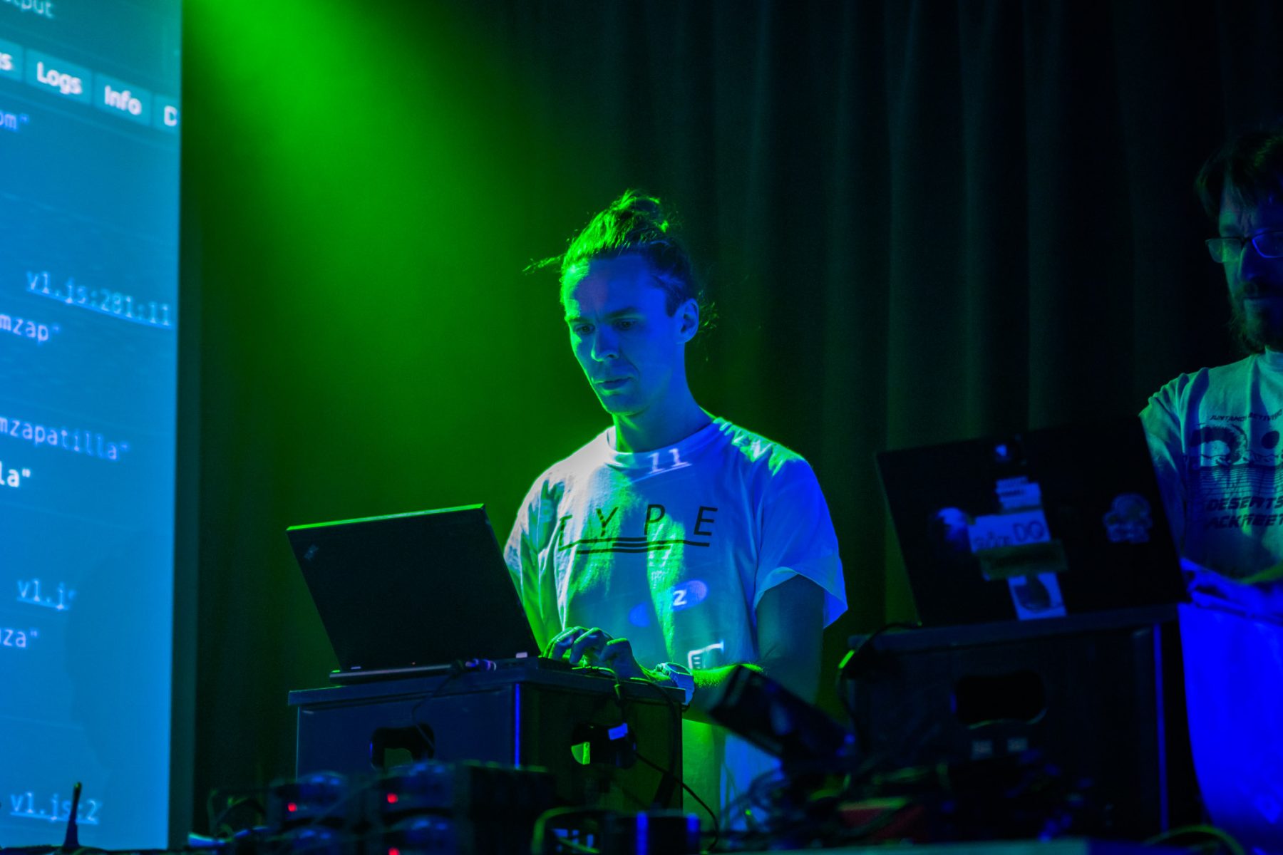 A person standing on stage under a light, performing with a laptop